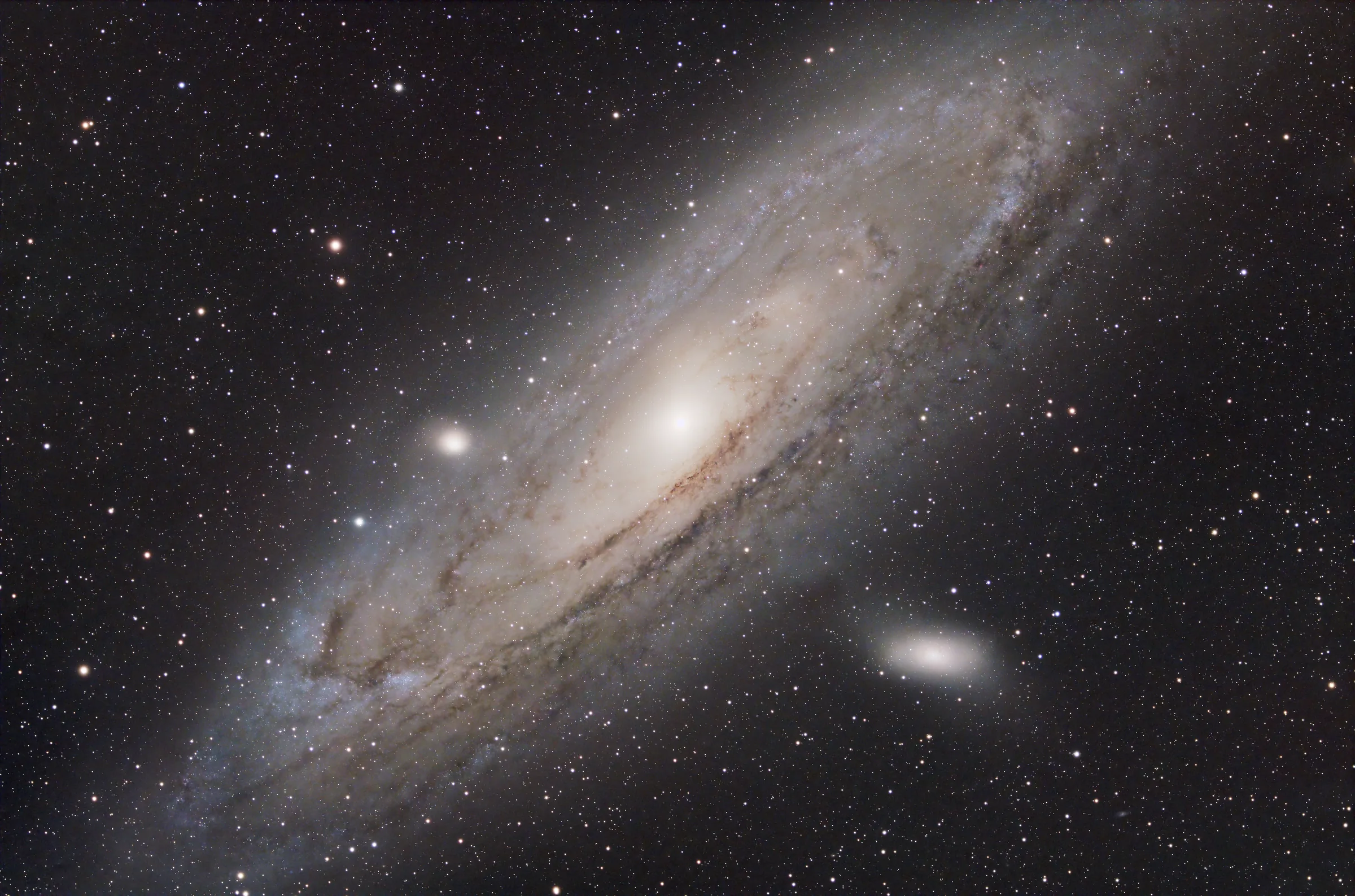 The Andromeda Galaxy, a large tilted spiral with dark dust lanes and two companion galaxies.